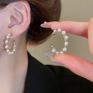 Close-up of C-shaped silver earrings with embedded pearls on a female model's ear