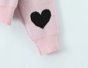 Detail shot of a pink knit sweater sleeve featuring a black heart pattern and ribbed cuff