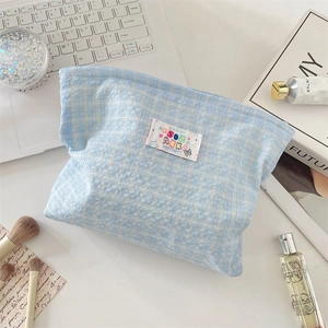 Detailed view of light blue checkered makeup bag with embroidered patches and bow