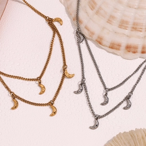 Détail de colliers superposés en or 18 carats et argent avec pendentifs lune sur fond coquillage