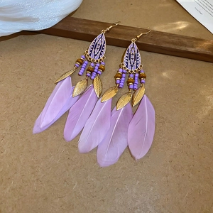 Detail of bohemian long feather earrings with light purple feathers and golden leaf