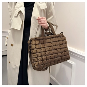Quilted puffer tote bag in brown fabric carried by model wearing a beige trench coat