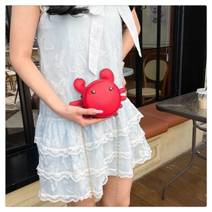 Red crab-shaped crossbody bag with a gold chain strap shown on a blue dress