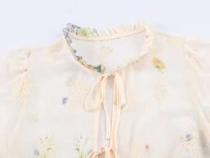 Detailed view of floral embroidery and lace trim on a beige French style blouse