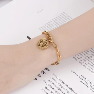 Gros plan d'un bracelet doré avec fermoir OT et pendentif Elizabeth porté par un mannequin