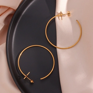 Close-up of golden hoop earrings featuring cross pendants on silk fabric background