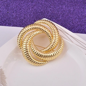 Abstract spiral hollow gold brooch on purple glitter background with white ceramic tray