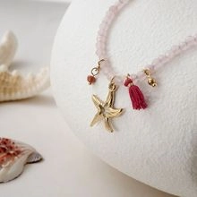 Detail of pink beaded necklace featuring golden starfish pendant and red fabric tassel