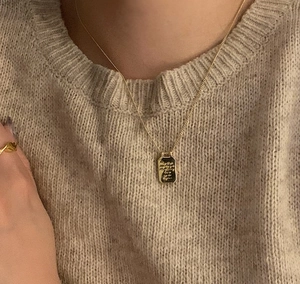 Close-up of golden rectangular pendant necklace worn on a warm beige sweater