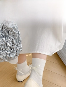 Close-up of cream knee-high socks with vertical ribbing and delicate satin bows