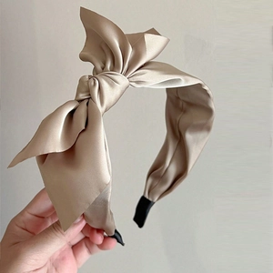 Detail of elegant double-layered oversized champagne satin bow headband held by hand