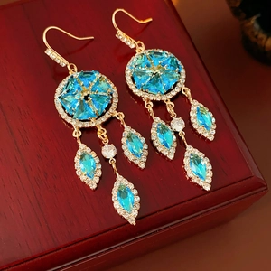 Detail of vintage gold earrings with blue gemstones and tassels on a wood surface