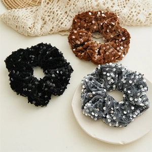 Detail of velvet sequin scrunchies in black, brown, and grey with glitter texture