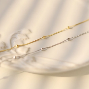 Close-up of gold and silver snake bone necklaces with small beads on a white ceramic plate