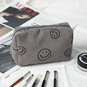 Gray corduroy cosmetic bag with black smiley faces shown with Vogue magazine and makeup tools