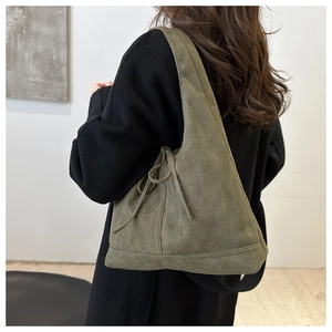 Detail of green suede shoulder bag with drawstring design worn on model's shoulder