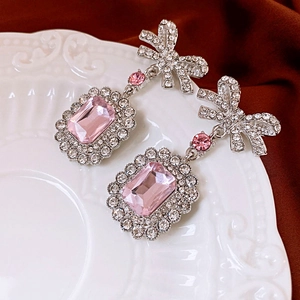 Macro detail of pink crystal bow earrings with rhinestone inlay on a white embossed plate