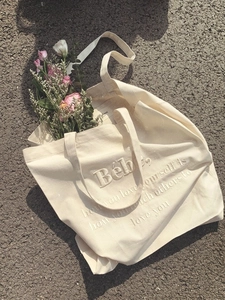 Detail der cremefarbenen Canvas-Tasche mit geprägtem Bébé-Schriftzug und Blumen