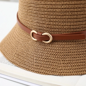 Straw sun hat with brown leather strap and gold buckle on a magazine background