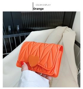Close-up of orange quilted silicone mini heart crossbody bag with gold chain strap