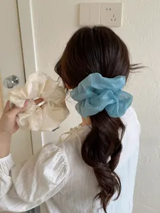 Dettaglio di elastici scrunchie giganti in rete a sirena color crema e azzurro in tessuto