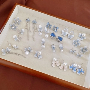 Close-up of blue crystal flower and pearl stud earrings arranged in a wooden jewelry box
