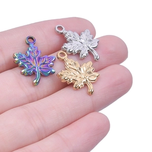Close-up of three maple leaf charms in gold, silver, and iridescent steel on a hand