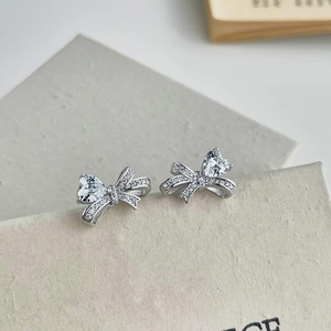 Macro detail of silver bow stud earrings with heart-shaped blue zircon stone
