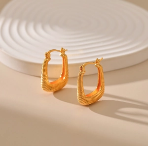 Macro detail of U-shaped gold earrings featuring textured spring-like surface and secure clasp