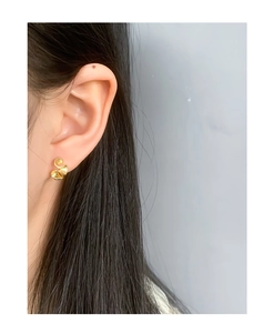Close-up of golden wavy ruffled stud earrings on model for a minimalist luxury look