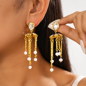 Close-up of gold tassel earrings with teardrop gems and white pearls on a model