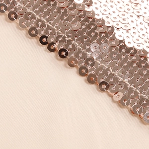 Macro shot of rose gold sequins on beige fabric showing detailed stitching and texture