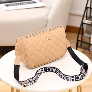 Beige quilted shoulder bag with wide woven strap and gold hardware on a table