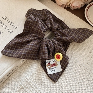Close-up of brown plaid fabric scrunchie with yellow button and cute dog patch detail