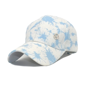 Detail of blue tie-dye baseball cap with a silver metallic 'M' emblem on the side