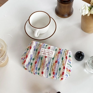 Top view of a woven tweed makeup bag on a white desk with decorative lifestyle props