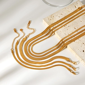 Close-up of golden flat snake chains on a stone step with soft shadow lighting