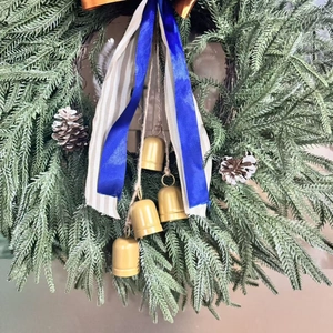 Artificial Christmas wreath with pine needles, cones, gold bells, and striped ribbon bow