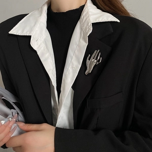 Polished silver hand brooch detail on a black suit lapel with liquid metal finish