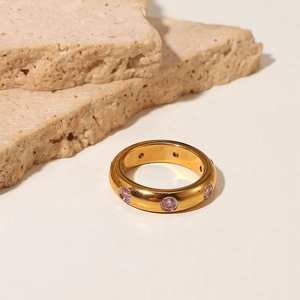 Detail view of a gold ring with pink circular gemstones on a textured stone base