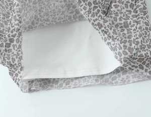 Detailaufnahme von grauem Netzstoff mit Leopardenmuster, weißem Futter und Saumnaht