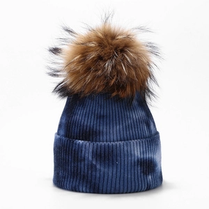 Close-up of blue tie-dye knit beanie featuring a large fluffy brown fur pom-pom detail