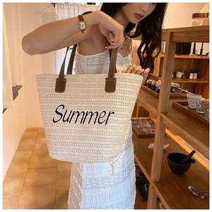 Beige woven straw tote bag with brown leather handles held in a warm interior setting