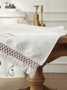 Detail of white jacquard table runner with leaf patterns and woven tassel fringe on wood