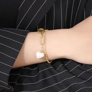 Close-up of golden double-layer chain bracelet with heart and pearl charms on wrist