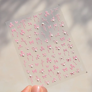 Detail of 3D embossed pink bow nail stickers with white pearl accents on clear sheet