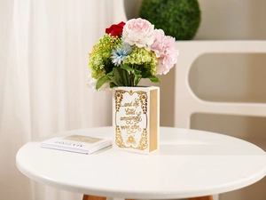Close-up of book-shaped ceramic vase with gold script and colorful faux flowers