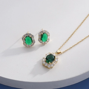 Detail of gold necklace and earrings set with green oval stone and white zircon stones