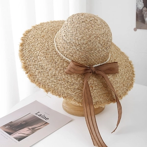 Dettaglio del cappello di paglia rafia con bordi grezzi, perline e fiocco di seta