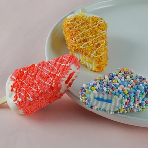 Three colorful simulation PU foam ice cream popsicles with wooden sticks on a white plate